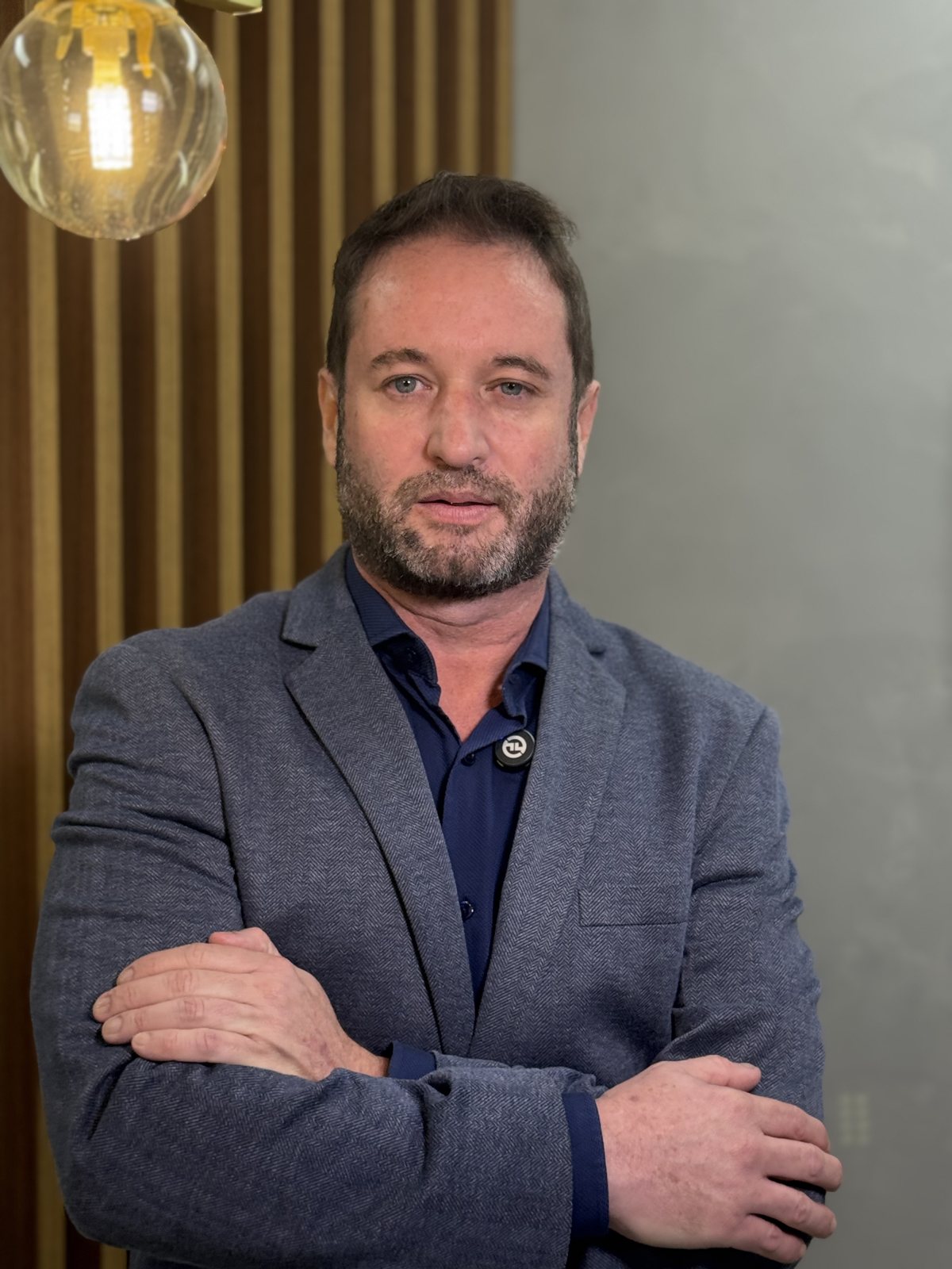 Dr. Marcos Vasquez em pé no consultório, de braços cruzados.